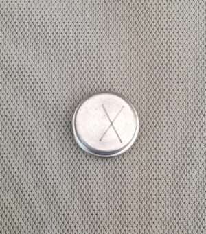 Silver button battery on gray fabric.