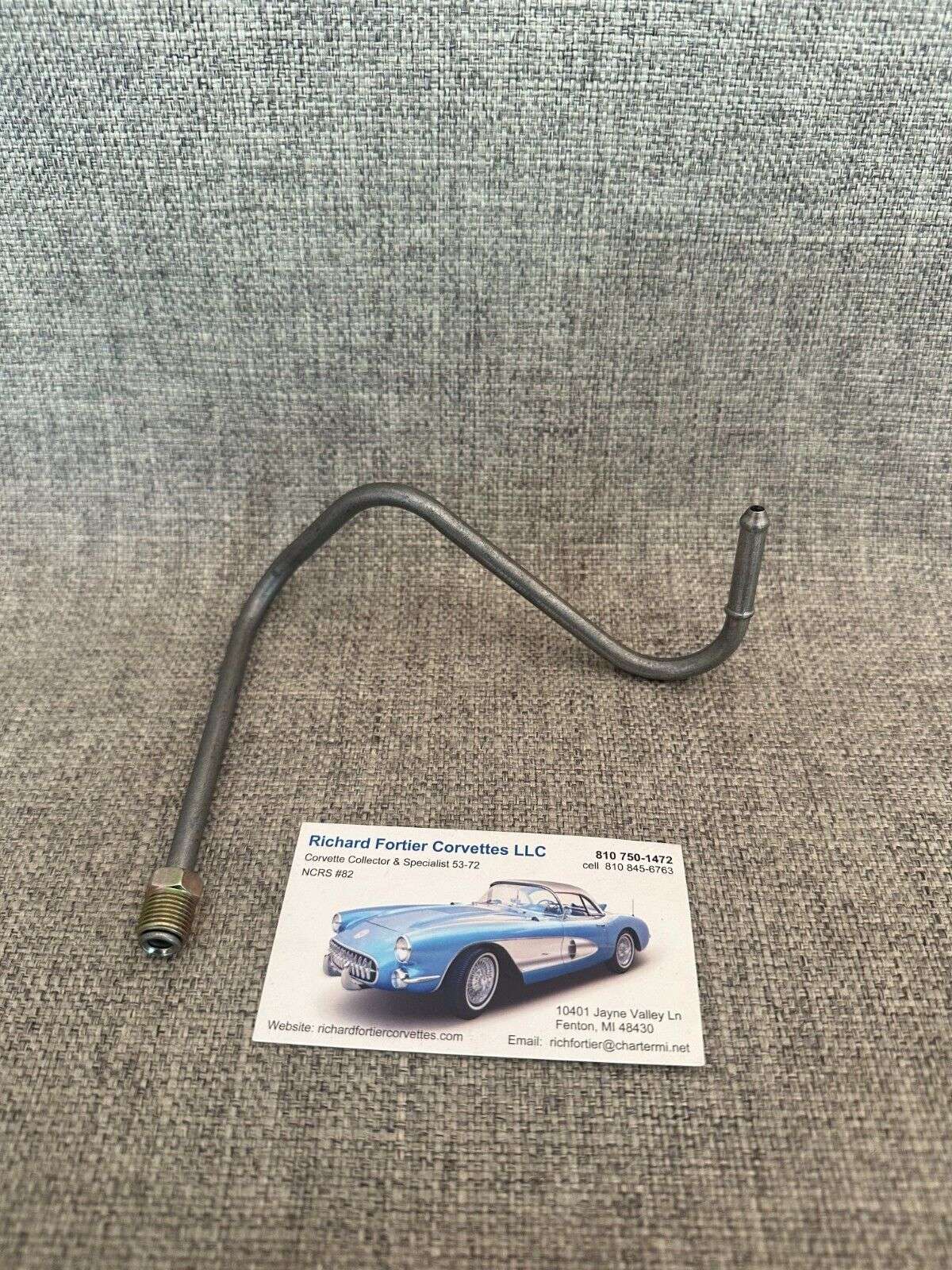 Car fuel line part and business card on fabric surface.